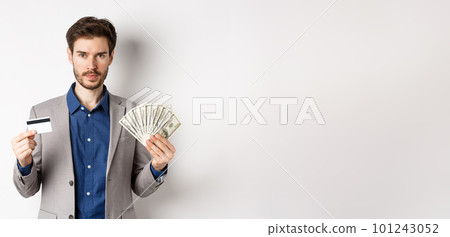 Successful businessman making money, standing in suit with dollar bills and plastic credit card, white background 101243052