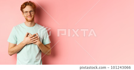 Attractive young man with ginger hair, holding hands on heart and smiling grateful, saying thank you, express gratitude, standing over pink background Attractive young man with ginger hair, holding hands on heart and smiling grateful, saying thank you, express gratitude, standing over pink background 101243066