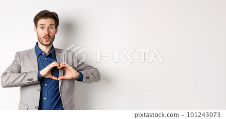 Handsome man looking silly, showing heart love you sign and pucker lips, waiting for kiss from lover, standing in suit on white background 101243073