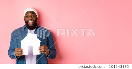 Real estate concept. Happy smiling african-american man holding house model, looking excited at camera, searching for home, standing over pink background Real estate concept. Happy smiling african-american man holding house model, looking excited at camera, searching for home, standing over pink background 101243183