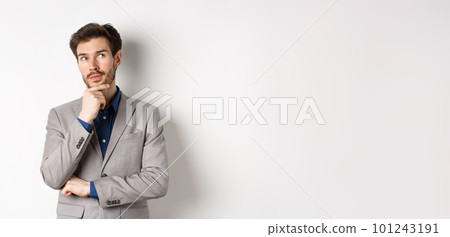 Pensive handsome man in suit looking up and thinking, making choice, pondering ideas, standing against white background 101243191