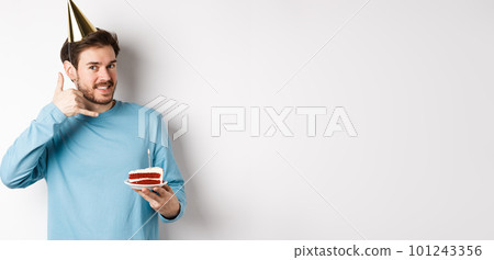 Celebration and holidays concept. Cheerful smiling man in party hat, celebrating birthday with bday cake, showing call me phone gesture near ear, white background Celebration and holidays concept. Cheerful smiling man in party hat, celebrating birthday with bday cake, showing call me phone gesture near ear, white background 101243356