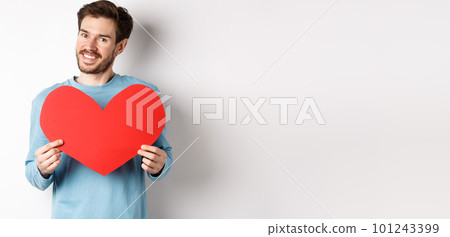 Handsome european man in sweater saying I love you, boyfriend standing with valentines day red heart, posing over white background 101243399