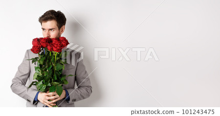 Romantic man in suit smell bouquet of roses and looking pensive, standing over white background. Concept of valentines day 101243475