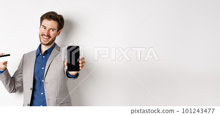 Online shopping. Successful businessman holding plastic credit card and showing mobile screen, smiling satisfied, making money, white background 101243477