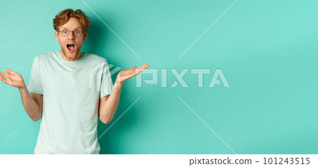 Surprised handsome man with red hair, wearing glasses, spread hands sideways and gasping in awe, looking wondered at camera, standing over turquoise background Surprised handsome man with red hair, wearing glasses, spread hands sideways and gasping in awe, looking wondered at camera, standing over turquoise background 101243515