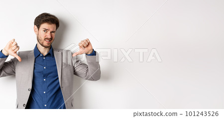 It sucks. Man feeling awkward showing thumbs down and judging something bad, frowning disappointed, standing in suit on white background 101243526