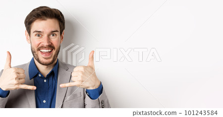 Excited salesman smiling, showing phone signs and asking to give him call, giving his number, standing on white background in suit 101243584