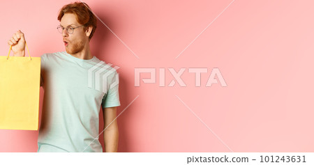 Handsome young man buying presents, holding shopping bag and looking amused, standing over pink background Handsome young man buying presents, holding shopping bag and looking amused, standing over pink background 101243631