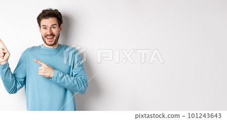 Happy caucasian man in casual blue sweatshirt, pointing fingers at upper left corner, showing link or logo on white background, smiling at camera Happy caucasian man in casual blue sweatshirt, pointing fingers at upper left corner, showing link or logo on white background, smiling at camera 101243643