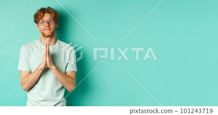 Cute redhead man asking for help, saying please with namaste gesture, pleading or begging for favour, looking silly at camera, standing over mint background 101243719