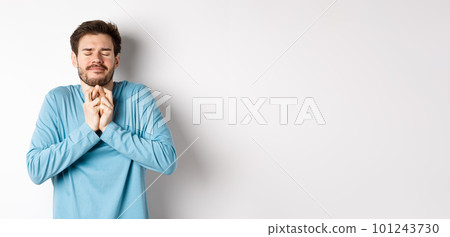 Hopeful caucasian guy in sweatshirt cross fingers for good luck. Young man making wish, praying with eyes closed and dreamy smile, standing over white background 101243730