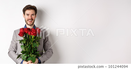 Excited handsome man in suit holding bouquet of roses for romantic date with lover, standing happy on Valentines day, white background 101244094
