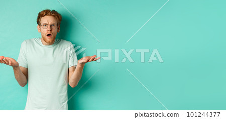 Confused and shocked guy with red messy hair and glasses, shrugging and raising hands, staring at something strange, cant understand, standing over turquoise background Confused and shocked guy with red messy hair and glasses, shrugging and raising hands, staring at something strange, cant understand, standing over turquoise background 101244377