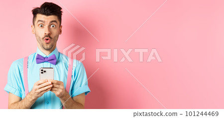 Online shopping. Intrigued guy in bow-tie, checking out internet promo offer on mobile phone, say wow at camera, holding smartphone, standing on pink background Online shopping. Intrigued guy in bow-tie, checking out internet promo offer on mobile phone, say wow at camera, holding smartphone, standing on pink background 101244469