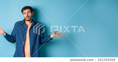 Indecisive young man with beard, look away and shrugging shoulders, know nothing, being clueless, standing on blue background 101244509