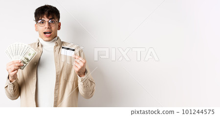 Excited young guy showing dollar bills and credit card, earn money and looking amazed, standing on white background Excited young guy showing dollar bills and credit card, earn money and looking amazed, standing on white background 101244575