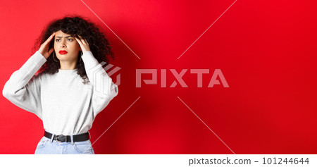 Distressed italian girl with curly hair, touching head temples and feeling bad, having headache, looking aside, standing on red background Distressed italian girl with curly hair, touching head temples and feeling bad, having headache, looking aside, standing on red background 101244644
