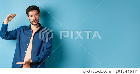 Modern guy showing big size, shaping large object and looking impressed at camera, standing on blue background Modern guy showing big size, shaping large object and looking impressed at camera, standing on blue background 101244687