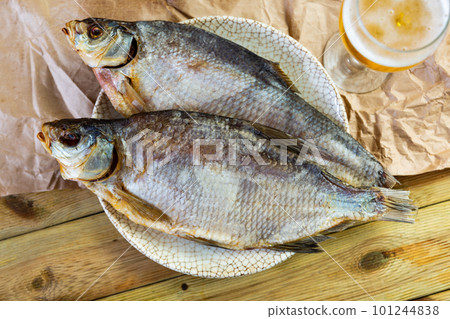 Dried bream lies on plate with imitation of antiquity. Fish complemented by glass of beer Dried bream lies on plate with imitation of antiquity. Fish complemented by glass of beer 101244838