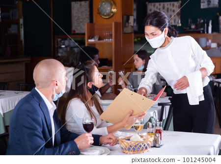 smiling female waiter taking order from couple in restaurante diring virus 101245004