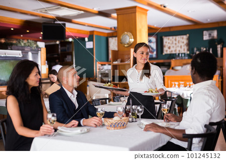 female waitress serving order to friends in modern restaurante 101245132