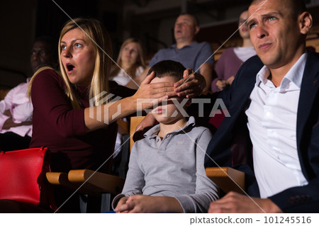 Woman closing eyes of preteen son while watching movie in cinema 101245516