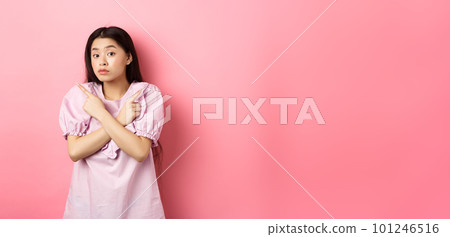 Clueless cute asian girl pointing sideways and look confused, cant make decision, standing hesitant against pink background 101246516