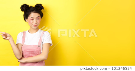 Glamour asian girl with bright makeup, pointing finger left and winking at camera, hint on good promo deal, standing on yellow background Glamour asian girl with bright makeup, pointing finger left and winking at camera, hint on good promo deal, standing on yellow background 101246554