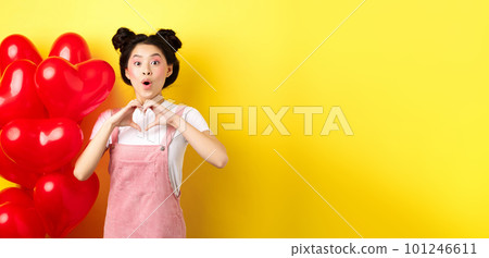 Surprised asian woman looking in awe, showing heart gesture, making love confession on valentines day, standing near romantic red balloons over yellow background Surprised asian woman looking in awe, showing heart gesture, making love confession on valentines day, standing near romantic red balloons over yellow background 101246611