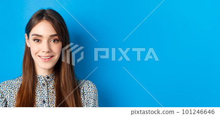 Close-up portrait of attractive natural girl with long hair and makeup, smiling happy and friendly at camera, blue background 101246646