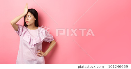 Annoyed asian girl roll eyes and facepalm, feeling tired and irritated with stupid conversation, standing against pink background 101246669