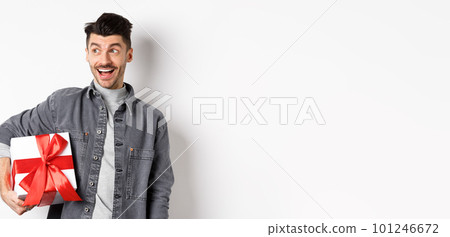 Cheerful handsome guy looking at empty space with amazed smile, checking out special valentines day offer, holding big romantic gift box, standing on white background Cheerful handsome guy looking at empty space with amazed smile, checking out special valentines day offer, holding big romantic gift box, standing on white background 101246672