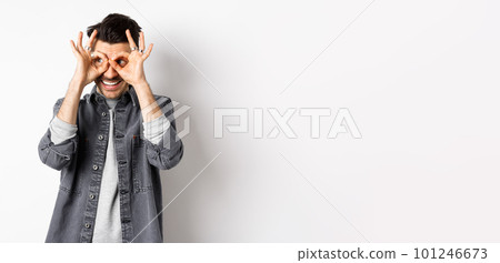 Smiling guy looking left at logo through hand binoculars, see good dea and look satisfied, standing on white background Smiling guy looking left at logo through hand binoculars, see good dea and look satisfied, standing on white background 101246673
