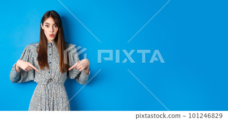 Excited beautiful woman in dress say wow, pointing fingers down and look amused, checking out promotion, standing on blue background Excited beautiful woman in dress say wow, pointing fingers down and look amused, checking out promotion, standing on blue background 101246829
