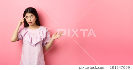 Are you stupid. Shocked asian woman pointing at head and complaining, scolding someone crazy or strange, look aside, standing against pink background 101247099