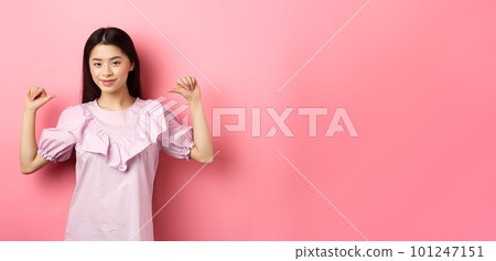 Confident asian girl smiling, pointing at herself, self-promoting personal achievements, standing in dress on pink background 101247151