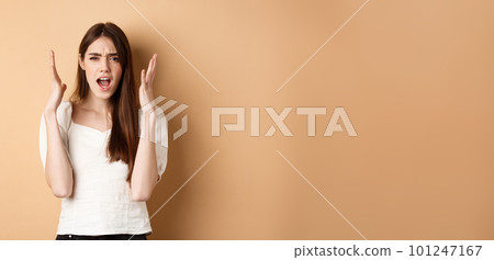 Frustarted woman shouting and shaking hands angry, looking mad, standing distressed on beige background 101247167