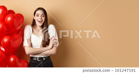 Valentines day concept. Beautiful young woman having fun, laughing and smiling at camera, standing near romantic heart balloons, beige background Valentines day concept. Beautiful young woman having fun, laughing and smiling at camera, standing near romantic heart balloons, beige background 101247191