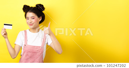 Shopping. Stylish asian glam girl showing thumb up and plastic credit card, standing on yellow background Shopping. Stylish asian glam girl showing thumb up and plastic credit card, standing on yellow background 101247202