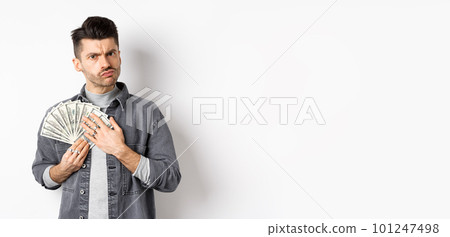 Greedy guy frowning and hugging dollar bills, unwilling to share money, standing on white background Greedy guy frowning and hugging dollar bills, unwilling to share money, standing on white background 101247498