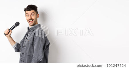 Profile of handsome smiling man holding mic, turn head at camera with excited face, singing karaoke and perform standup, standing on white background Profile of handsome smiling man holding mic, turn head at camera with excited face, singing karaoke and perform standup, standing on white background 101247524