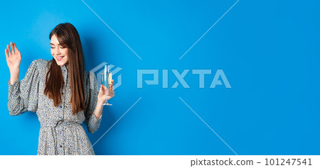 Celebration and party concept. Dancing girl holding glass of champagne, having fun at holiday, celebrating birthday, standing on blue background Celebration and party concept. Dancing girl holding glass of champagne, having fun at holiday, celebrating birthday, standing on blue background 101247541