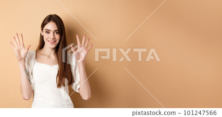 Attractive young woman show fingers number ten, smiling and looking confident, standing on beige background 101247566