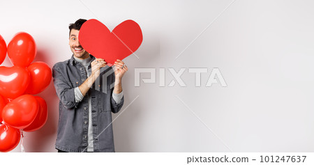 Romantic smiling man cover face with Valentine heart card and looking happy at camera, celebrating lovers day with partner, standing on white background Romantic smiling man cover face with Valentine heart card and looking happy at camera, celebrating lovers day with partner, standing on white background 101247637