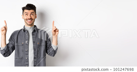Cheerful caucaisan man with moustache pointing and looking up, smiling dreamy, showing cool promotion deal, standing on white background 101247698