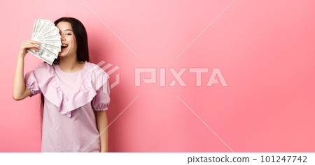 Happy rich asian woman showing money and smiling, shopping with cash, standing in dress against pink background Happy rich asian woman showing money and smiling, shopping with cash, standing in dress against pink background 101247742
