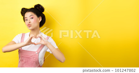 Silly japanese girl showing heart gesture and wishing happy Valentines day, pucker lips to kiss lover, standing on yellow background Silly japanese girl showing heart gesture and wishing happy Valentines day, pucker lips to kiss lover, standing on yellow background 101247802