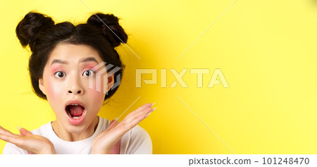 Close-up of excited asian woman with glamour makeup and hairstyle, screaming of amazement, open mouth and look at camera in awe, yellow background 101248470
