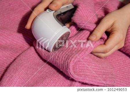 Woman using Anti-pilling razor at home. Device for shaving clothes. Anti-Plush fabric Shaver. Electric portable sweater pill defuzzer Lint remover from pink acrylic or wool sweater. Slow fashion 101249053